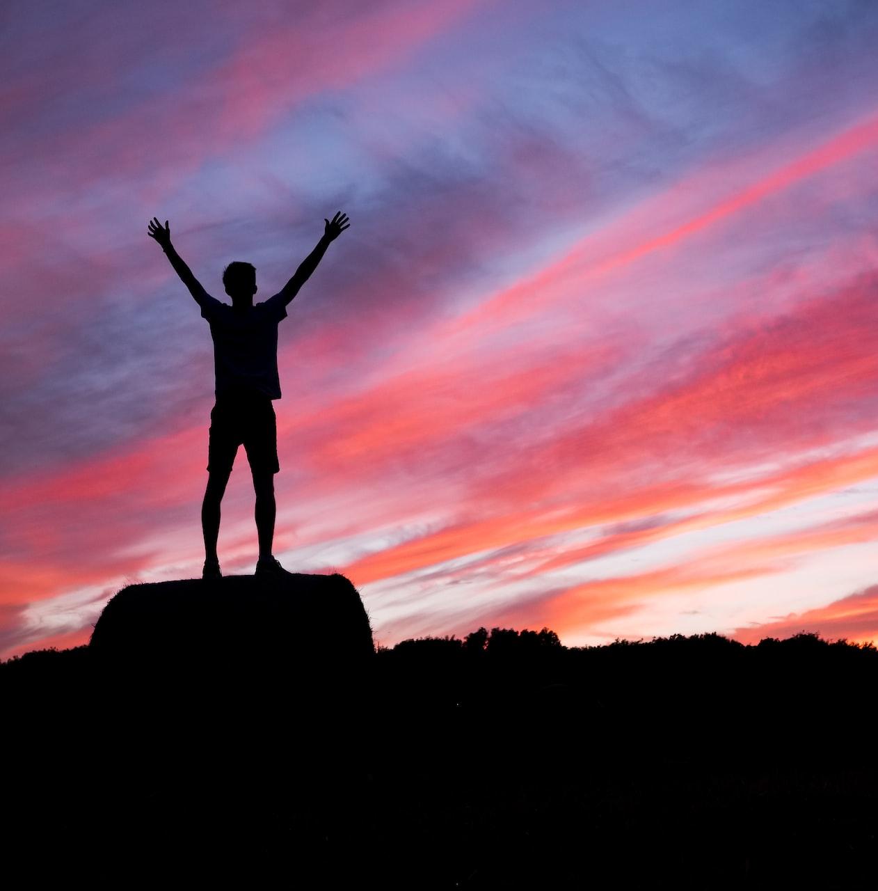 silhouette of man standing on high ground under red and blue skies