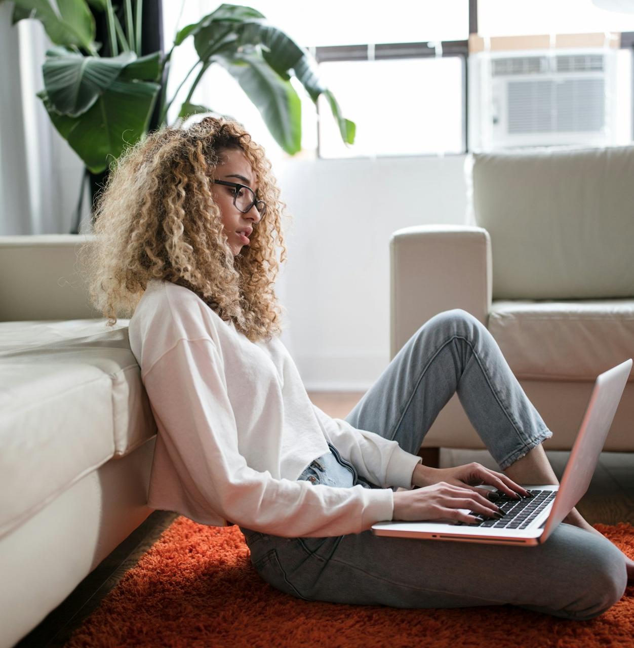 woman sitting on floor and leaning on couch using laptop